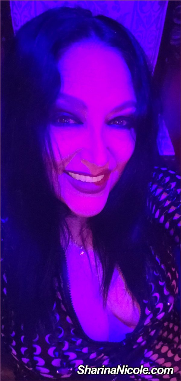 Minnesota Dominatrix Mistress Sharina Nicole smiling in mood lighting with a peekaboo jumpsuit Minnesota Dominatrix Mistress Sharina Nicole smiling in mood lighting with a peekaboo jumpsuit